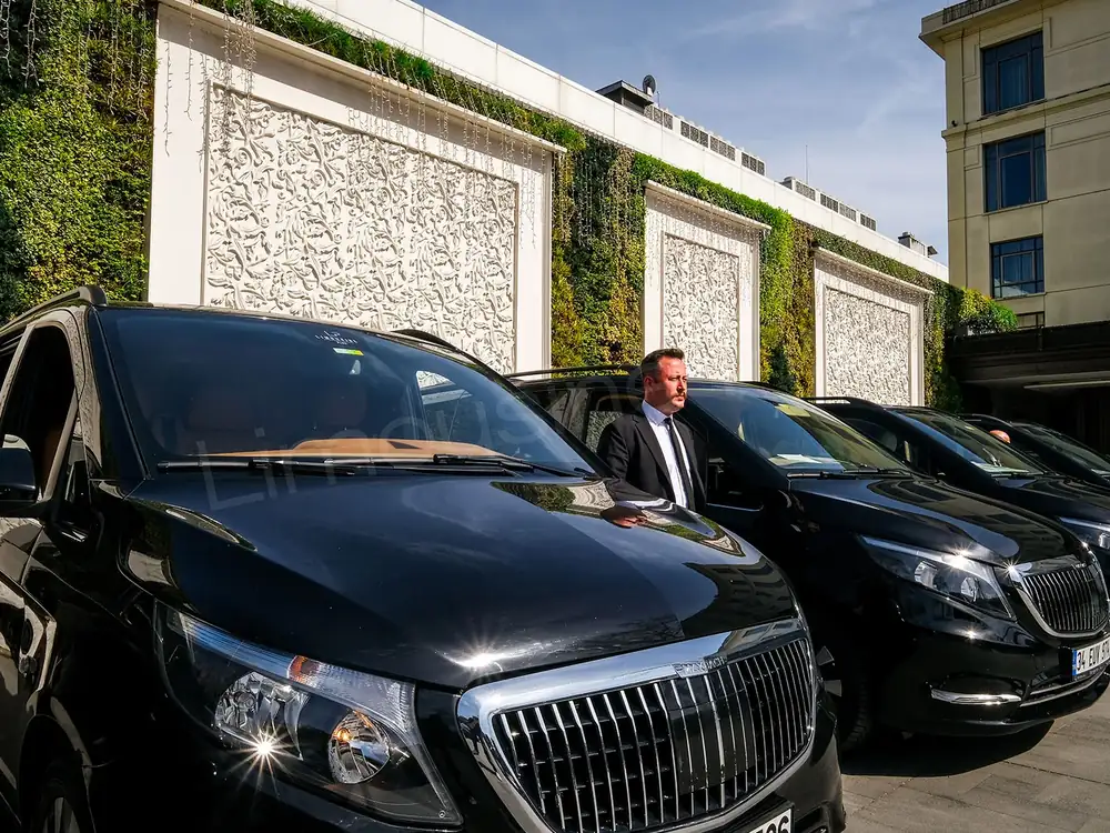 Limousine Plus chauffeur beside a black Mercedes Vito at a hotel entrance