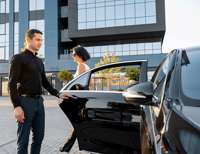 A professional Limousine Plus chauffeur holding the door for a female executive, providing a corporate transfer service in front of an office building in Istanbul.
