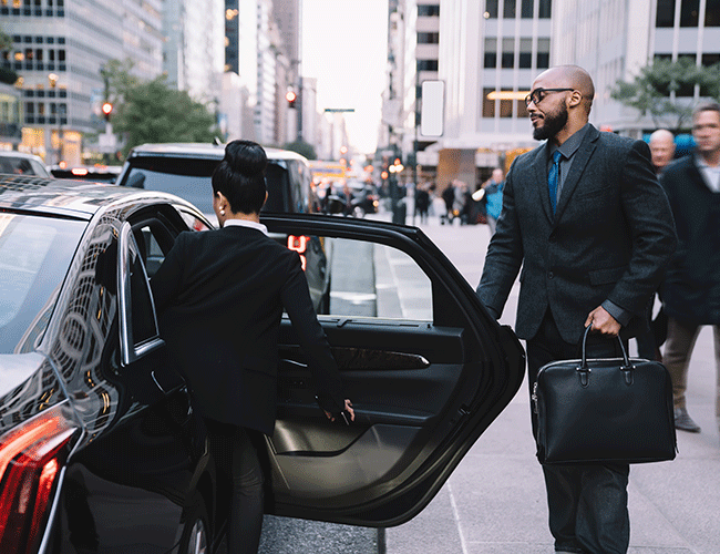 A chauffeur holding the car door open for a businessman with a briefcase, demonstrating Limousine Plus's executive VIP car service in a bustling city.